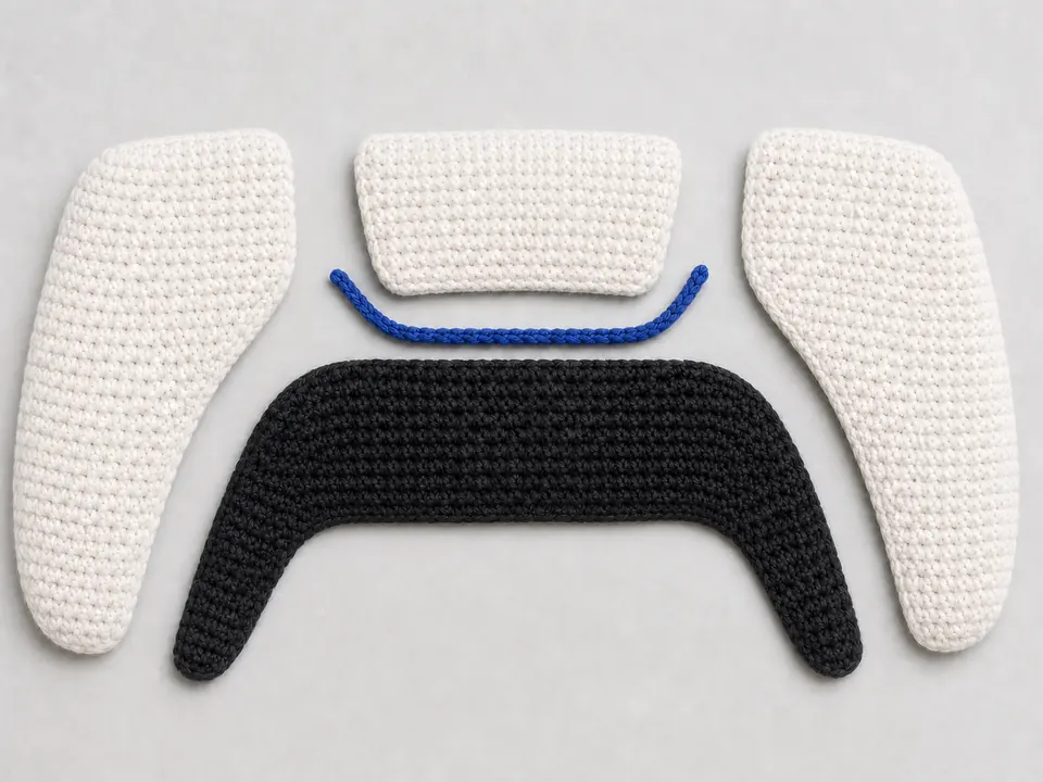 Crochet game controller construction with black base, white side shells, gray controls, and blue trim arranged before assembly